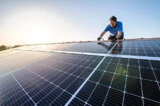 Mann installiert auf einem Dach eines Eigenheims eine Photovoltaikanlage. 